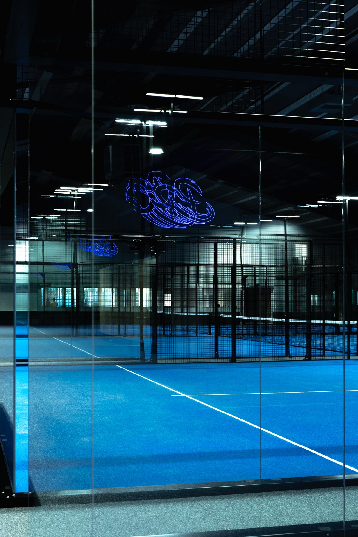 Blick durch die Glaswand auf die Courts mit Neonlogo